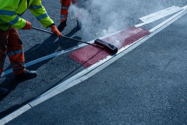 Yeni kavşak ve yol inşaatı sırasında yeni döşenmiş asfalt üzerinde termoplastik yol işareti uygulayan yol işçisi