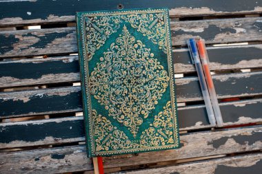 green notebook, pens on a wooden table in a cafe