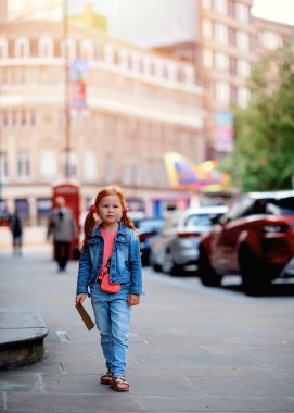 a cheerful smiling red-haired girl in a denim jacket walking around the city and having a fun