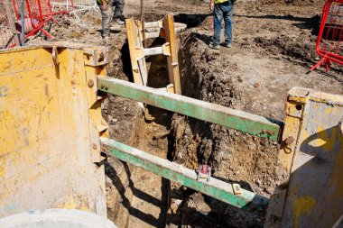 Ground workers installing trench support safety shoring system during deep drainage works on new residential housing development construction site