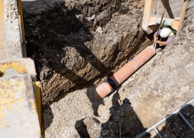 Ground workers installing new clay drainage pipe during deep drainage works on new residential housing development construction site
