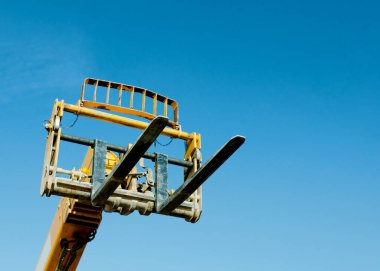 Telehandler with raised boom and forks on clear blue sky background