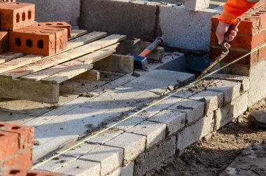 Bricklayer laying bricks and blocks on mortar on new residential house construction