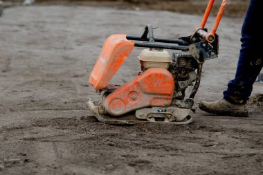 Construction worker using petrol powered plate compactor to compact stone during footpath construction on new residential development construction site