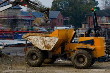 Houses under construction and excavator loading dumper with stone in front of them