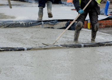 Construction workers pouring wet self leveling concrete screed during ground floor construction of a new residential house and spreading it with spazzle