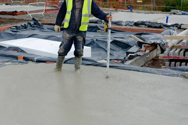 Concreter checking level of the concrete using laser level and staff as he pour ground floor slab of the new residential house
