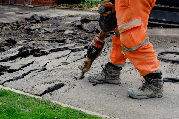 Construction worker breaking road gully using hydraulic breacker during road works on new housing development construction site