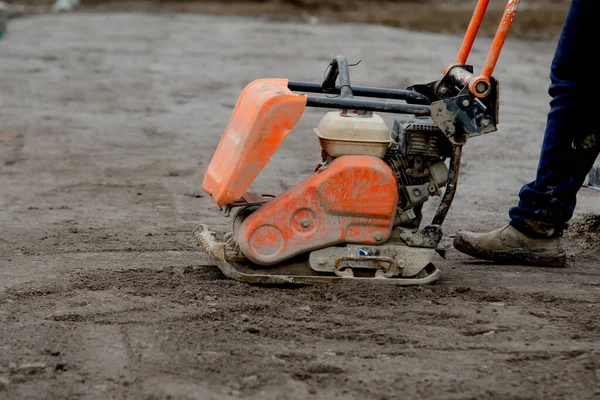 Construction worker using petrol powered plate compactor to compact stone during footpath construction on new residential development construction site