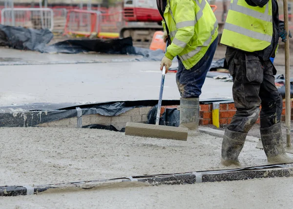 Construction workers pouring wet self leveling concrete screed during ground floor construction of a new residential house and spreading it with spazzle
