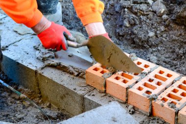 Turuncu hi-viz 'deki tuğla ustası inşaat alanına tuğla döşüyordu