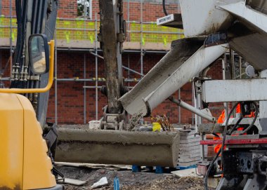 İnşaat alanındaki beton yığınına getirmek için içi ıslak beton dolu kazıcı kovası.