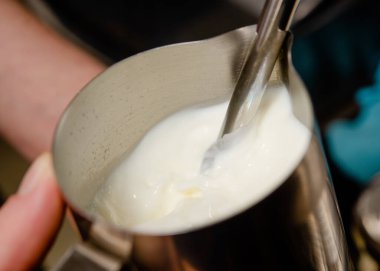 Kahve makinesinde kahve yapan bir barista kahve makinesinde süt karıştırıyor.