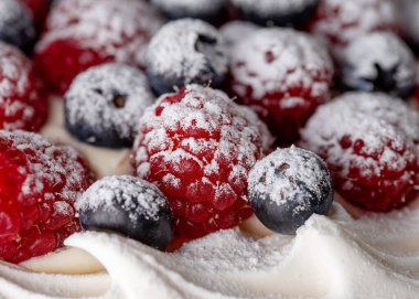 Yeşil zemin üzerinde yaban mersini ve ahududu olan kremalı pasta.