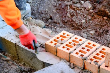 Turuncu hi-viz 'deki tuğla ustası inşaat alanına tuğla döşüyordu