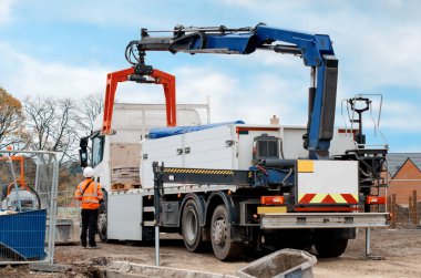Dropside plakalı HIAB vinç kamyonu tuğla kapma eklentisiyle inşaat alanına malzeme getiriyor ve indiriyor.
