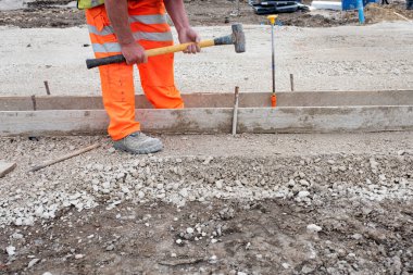 Yeni yol inşaatı sırasında iskele tahtaları ve çelik yol çivileri kullanarak kaldırıma zemin oluşturmak için beton kaplama yapan bahçıvan.