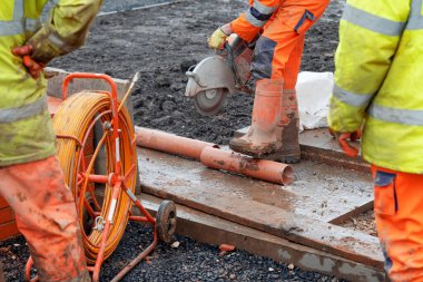 Saha çalışanları plastik boruları beton testereyle kesiyorlar.