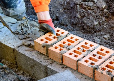 Turuncu hi-viz 'deki tuğla ustası inşaat alanına tuğla döşüyordu