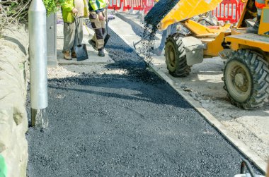 İnşaat işçileri yol çalışmaları ve yol onarımı sırasında sıcak asfalt döşüyorlar.