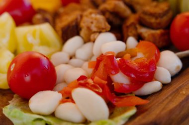 Kiraz domatesleri, tatlı biber, salatalık turşusu, sarımsak turşusu, zeytin, sosis, farklı peynir, ahşap tabakta pastırma. Atıştırmalık