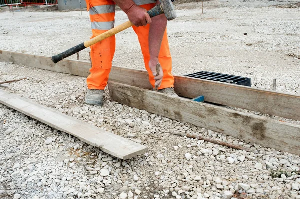 Yeni yol inşaatı sırasında iskele tahtaları ve çelik yol çivileri kullanarak kaldırıma zemin oluşturmak için beton kaplama yapan bahçıvan.