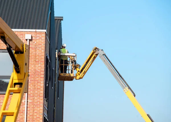 Builders working off Telescopic Boom Lift while fitting insulated sandwich panels to the facade of a new multistorey residential building. Working at height safely