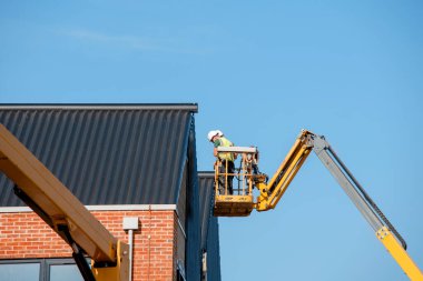 Teleskopik Patlama Asansörü 'nde çalışan inşaatçılar, izole edilmiş sandviç panellerini çok katlı yeni bir binanın ön cephesine yerleştiriyorlar. Güvenli bir şekilde çalışıyor.