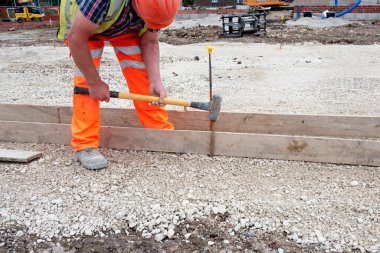 Yeni yol inşaatı sırasında iskele tahtaları ve çelik yol çivileri kullanarak kaldırıma zemin oluşturmak için beton kaplama yapan bahçıvan.
