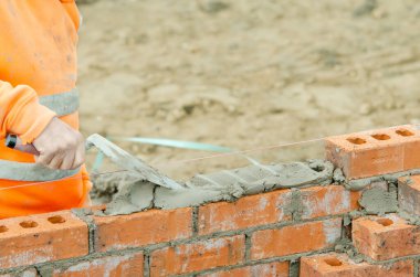 Yeni konut inşaatına tuğla döşeyen tuğla ustası.