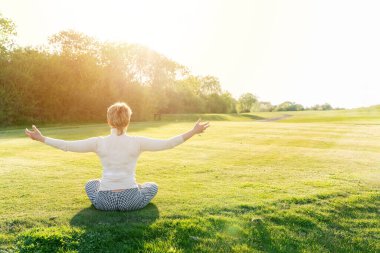 Güneşli bir bahar gününde çimlerde meditasyon yapan bir kadın.