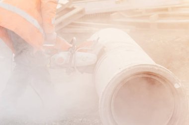 İnşaat alanında beton drenaj borusunu beton testereyle kesen bir işçi.