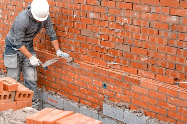 Bricklayer laying bricks on mortar on new residential house construction