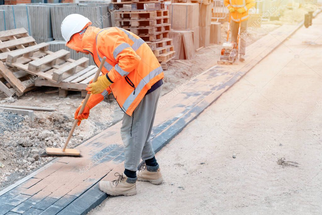 Construction workers filling joints of the block paved footpath with