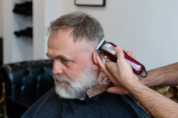 An old man enjoing haircut by a master in a barbershop.  An old man gets a stylish haircut