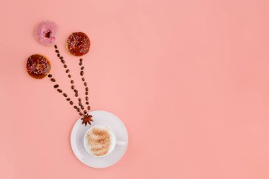 Bir fincan kahve, fasulye ve pembe arka planda üç çörek. Mesaj için yer var.