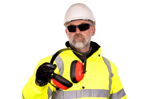 在嘈杂的环境中 戴着白色帽子 黄色的高维兹外套和深色的白色背景安全眼镜的建筑工人为观看者提供了充满泡沫的填充耳罩 — 图库照片