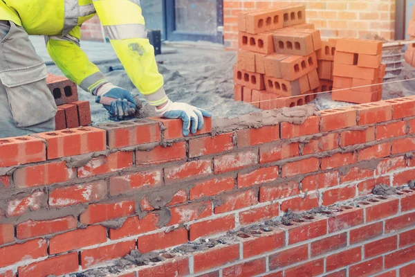 Güvenlik yeleği ve tuğla duvar döşeyen bir miğfer giyen bir duvar ustası.