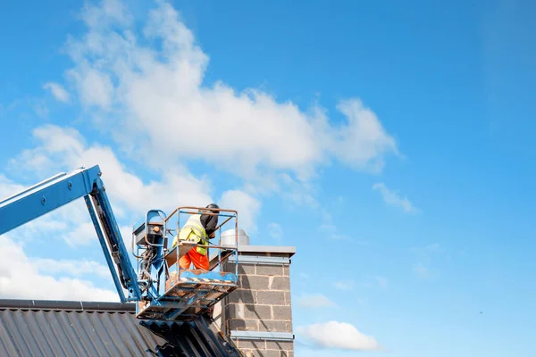 Builders working from Telescopic Boom Lift while fitting thermal insulated sandwich panels to the facade of a new multistorey residential building. Working at height safely