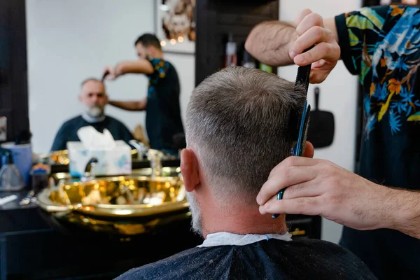 An old man enjoing haircut by a master in a barbershop.  An old man gets a stylish haircut
