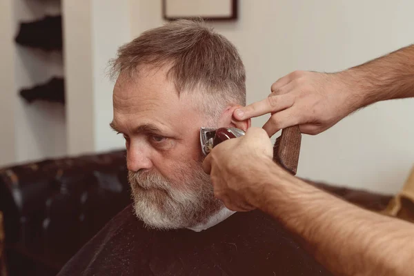 An old man enjoing haircut by a master in a barbershop.  An old man gets a stylish haircut