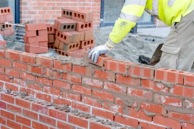Güvenlik yeleği ve tuğla duvar döşeyen bir miğfer giyen bir duvar ustası.