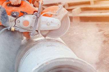 İnşaat alanında beton drenaj borusunu beton testereyle kesen bir işçi. İnşaat alanında güvenlik prosedürü ihlal edilirken tehlikeli bir toz bulutuyla kaplı bir bina..
