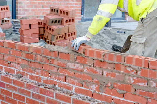 Güvenlik yeleği ve tuğla duvar döşeyen bir miğfer giyen bir duvar ustası.