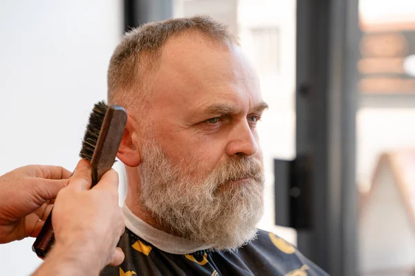 An old man enjoing haircut by a master in a barbershop. An old man gets a stylish haircut