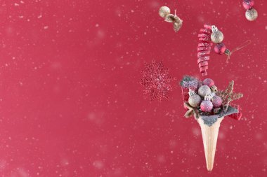 Dondurma külahında noel süslemesi kar bardağının arkasında kırmızı arka planda.