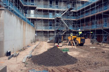 İnşaatçı, yeni inşaat alanına çöp kamyonu ve kazıcı sürüyor. İnşaat alanındaki araştırma ekipmanları