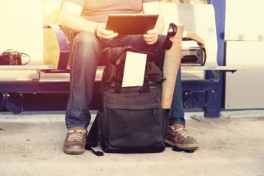 İnsan ve yeşil seyahat çantası, şapka, harita, güneş batarken tren istasyonundaki platformda duran gözlük.