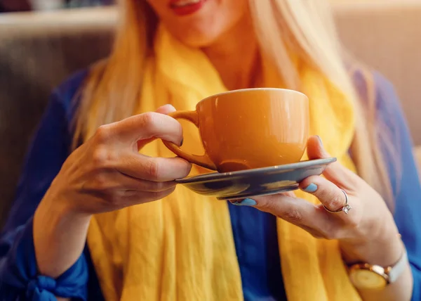 woman in a blue blouse and yellow scarf drinking coffee in the cafe.  Thinking about Ukraine