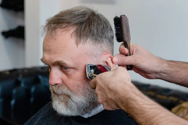 An old man enjoing haircut by a master in a barbershop.  An old man gets a stylish haircut